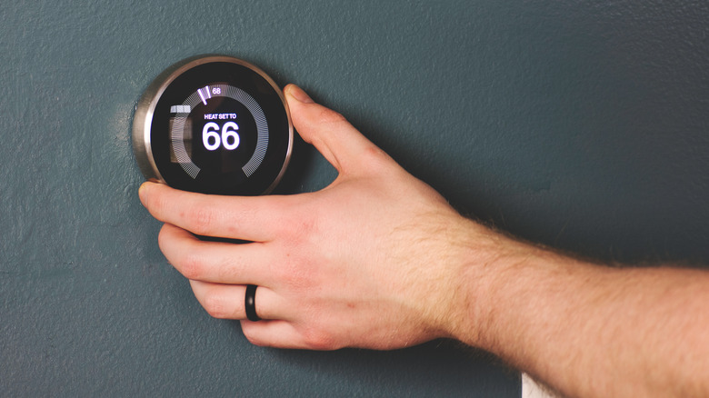 man adjusting his home thermostat to 66 degrees Fahrenheit