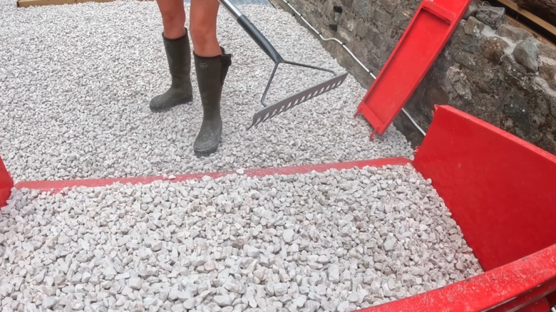 A person in red shorts and black boots raking a new gravel driveway installation at home