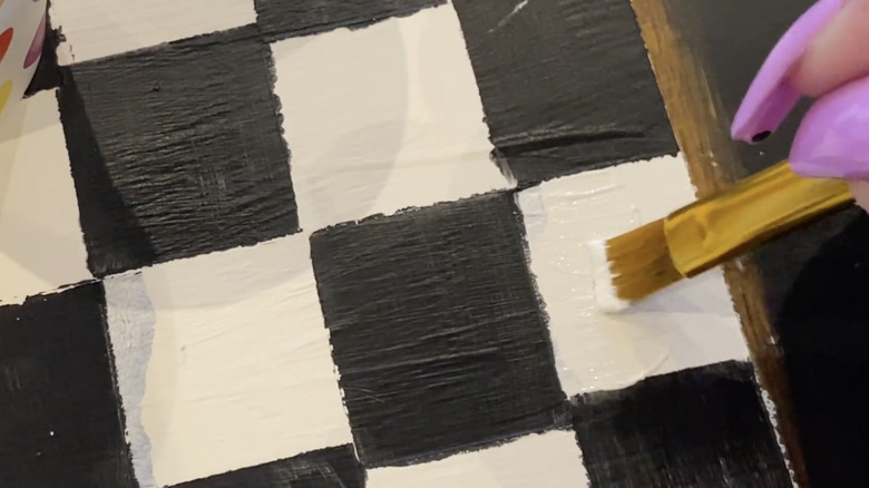 A person hand paints a black and white checkered design
