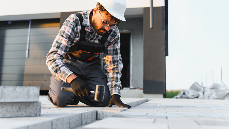 A man uses a rubber mallet to create a paver patio