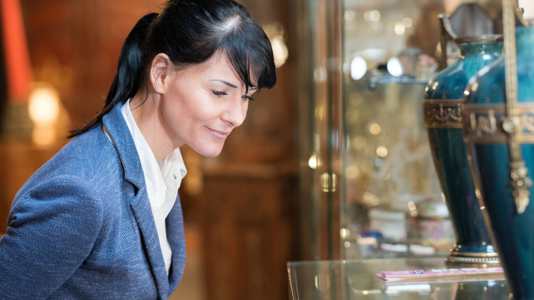 A woman looking at vases through the window of an antique shop