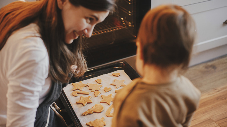 A woman taking cookies out of the oven and showing to a child