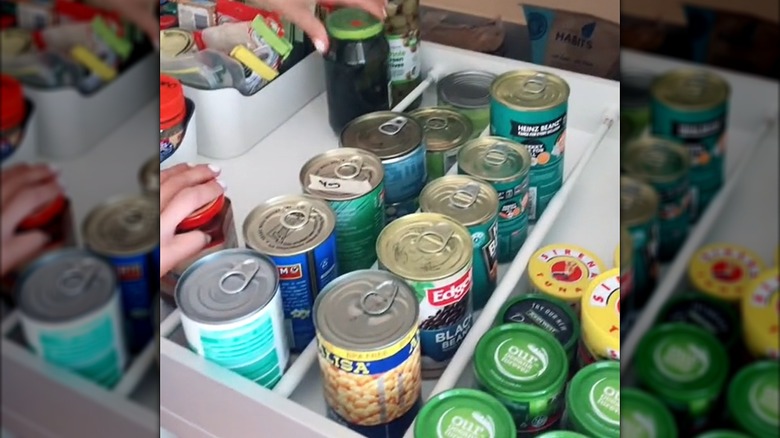 Woman stacking canned pantry items in deep drawer divided with white tension curtain rods
