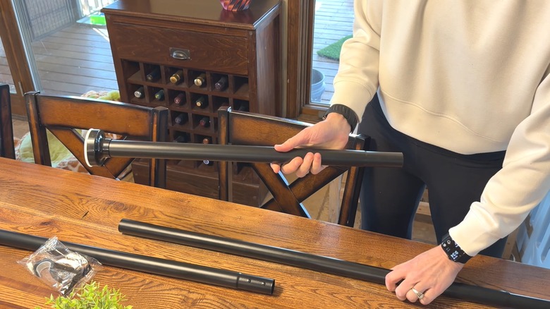 Woman assembling tension curtain rod over wood table in rustic style room