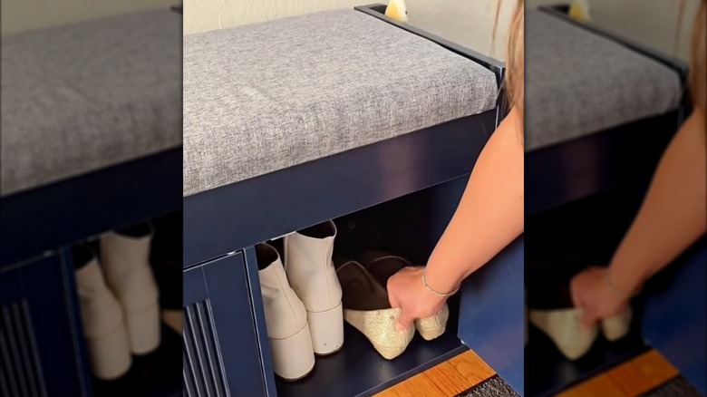 Woman storing formal flats beside white boots in blue and gray shoe cabinet storage bench