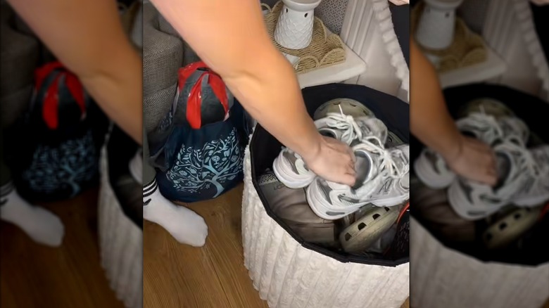 Woman storing household shoes in white fluted ottoman in cluttered living room