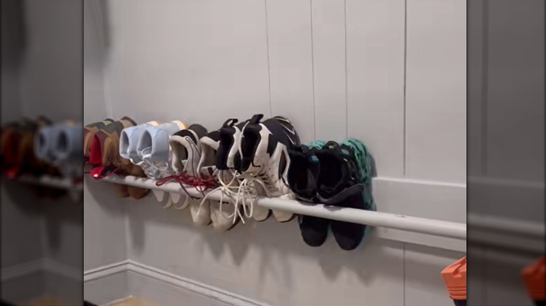 Assorted high-tops and hiking boots propped above floor with white DIY dowel rail