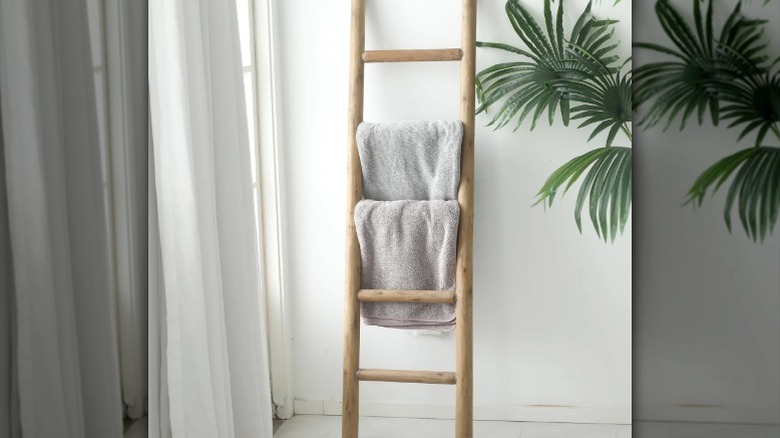 A rustic ladder towel rack leaning against the wall in a bathroom