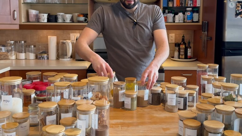 Young man cleaning out massive spice collection in decanted wood lid bottles on wood countertop