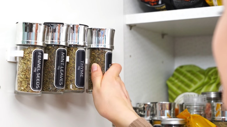 Young woman hanging decanted spice jars on white gripper clips inside cabinet door