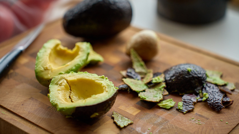 an avocado split open on a wooden cutting board.