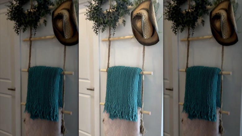 A DIY blanket ladder made from jute string and wooden dowels holding a pink and teal blanket