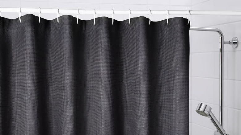 A black shower curtain hangs from a white rod hooks