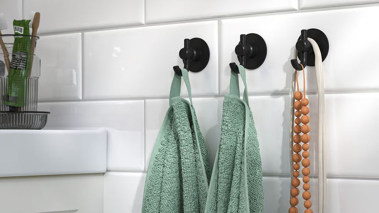 Two green bathroom towels hang on a set of black VALASJÖN Self-Adhesive Hooks from IKEA