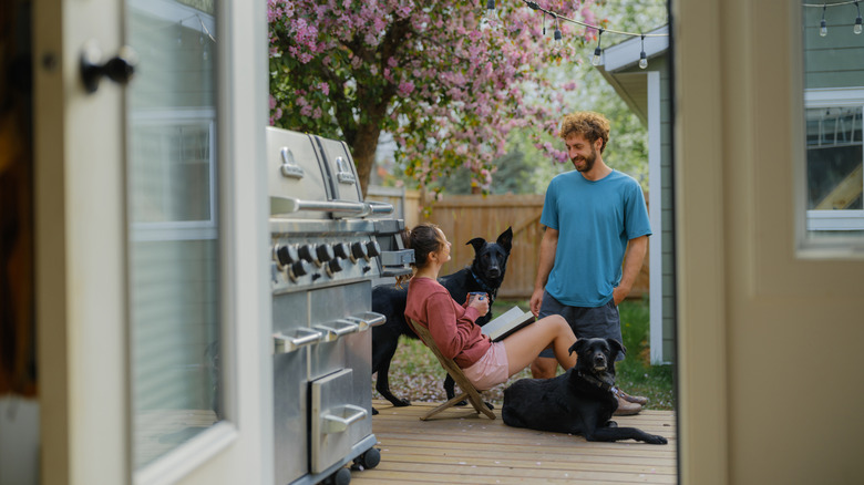 A couple smiles in a backyard with their dogs, with a fence in the background