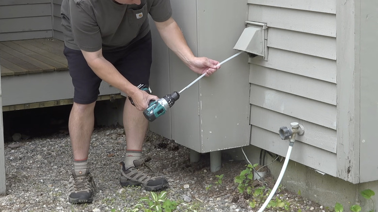 Homeowner using drill attachment to clean dryer vent from outside