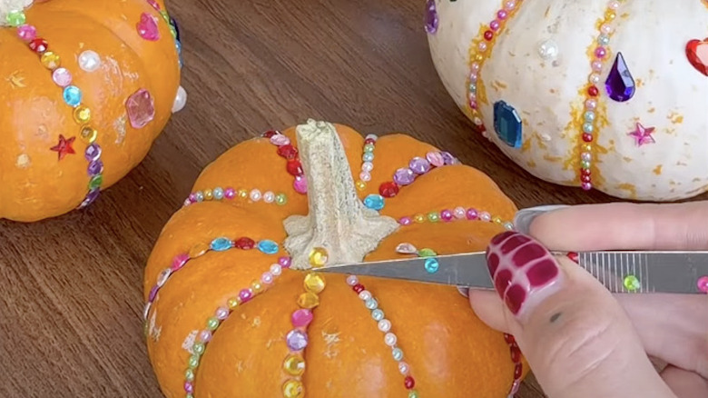 A person adhering gems and rhinestones onto pumpkins