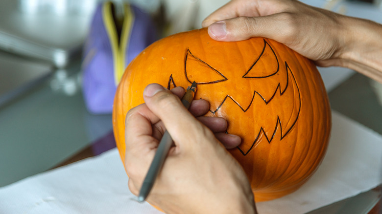 Someone drawing an outline of a scary face on a Halloween pumpkin