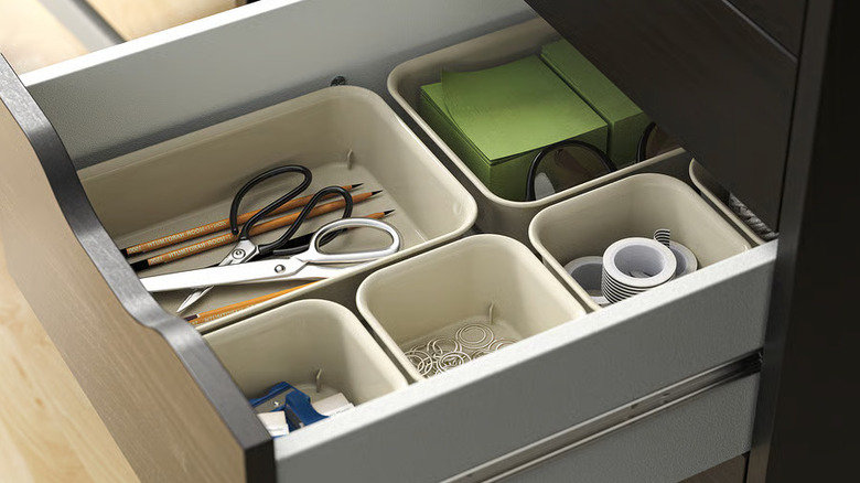 Several cream-colored plast NOJIG Organizers holding scissors and other supplies are arranged in a drawer