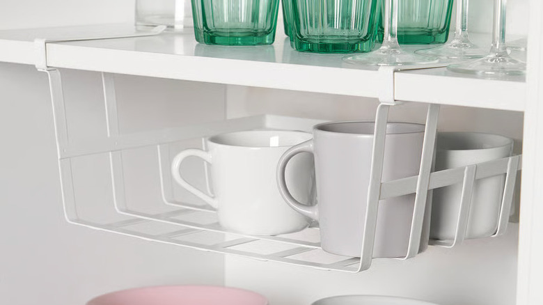 White coffee mugs are arranged inside a clip-on storage basket inside a pantry