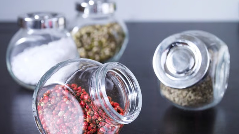 Four glass spice jars sit on a black countertop
