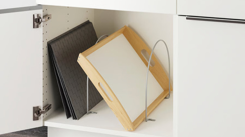 Two partitions separate a wooden tray and gray trivets in a kitchen cupboard