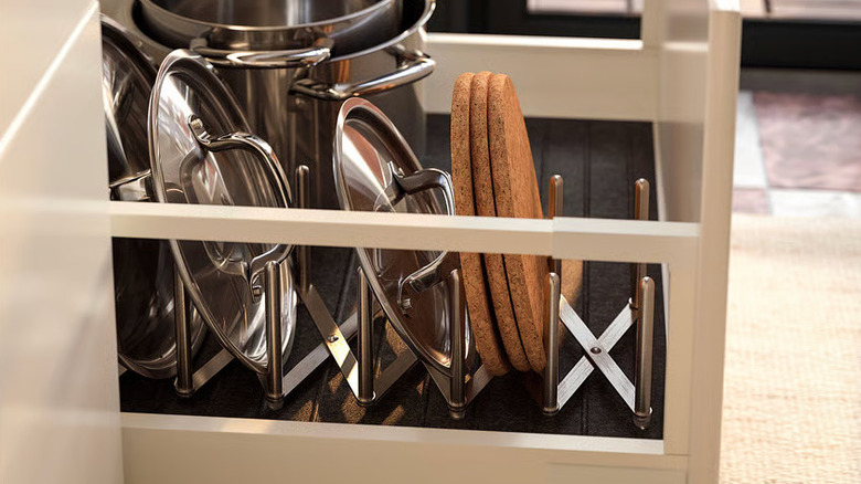 Stainless steel lids and cork coasters are sorted on a pot lid organizer in a kitchen drawer