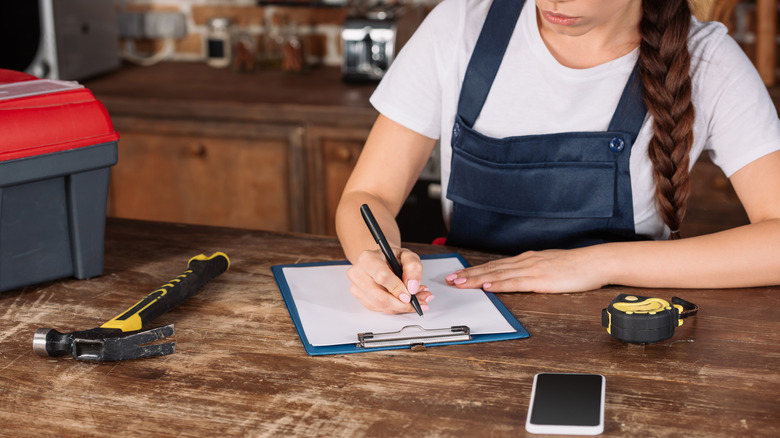 repairwoman writing something down with hammer and ruler tape and phone in foreground