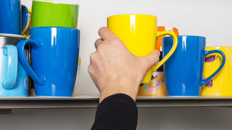 A hand taking a mug out of crowded cabinet