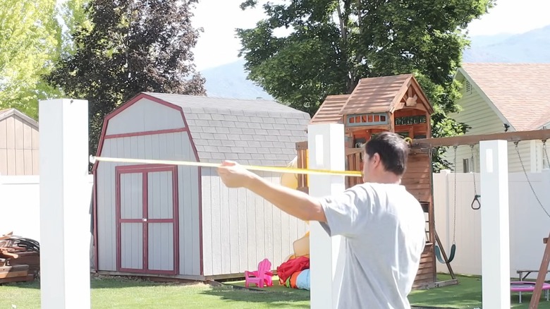 Man ensuring fence posts for DIY privacy screen are spaced correctly for private backyard with playground