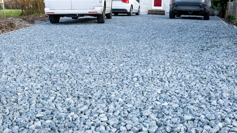 A close-up of a crushed granite driveway with cars in the background.