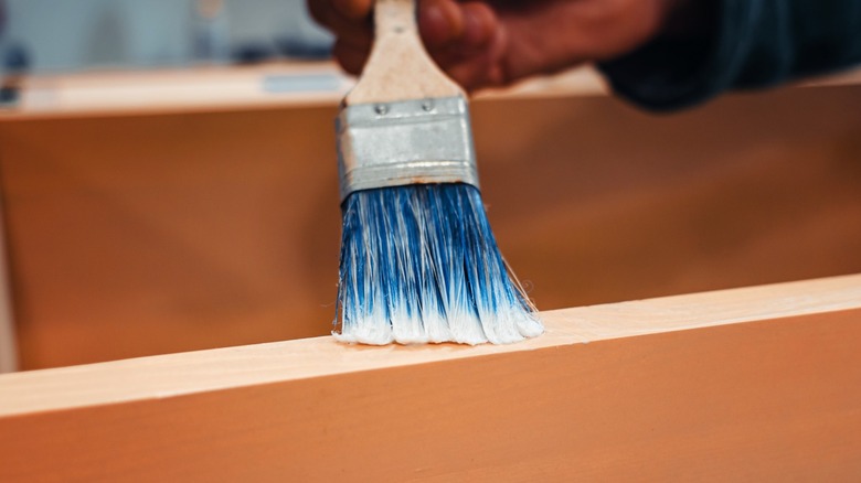 Person brushing varnish on the edge of a piece of wood