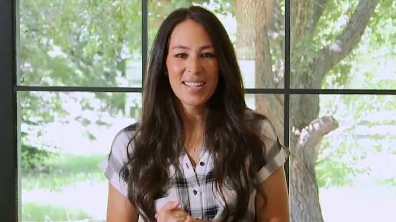 A woman (Joanna Gaines) with dark brown hair wearing a checked shirt smiling