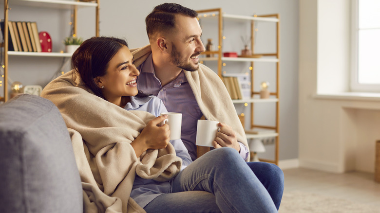 Couple on couch wrapped in throw blanket