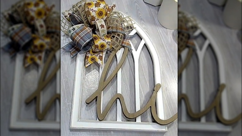 Front door decor made with an arched window frame piece with a large bow and the word "hi" on it