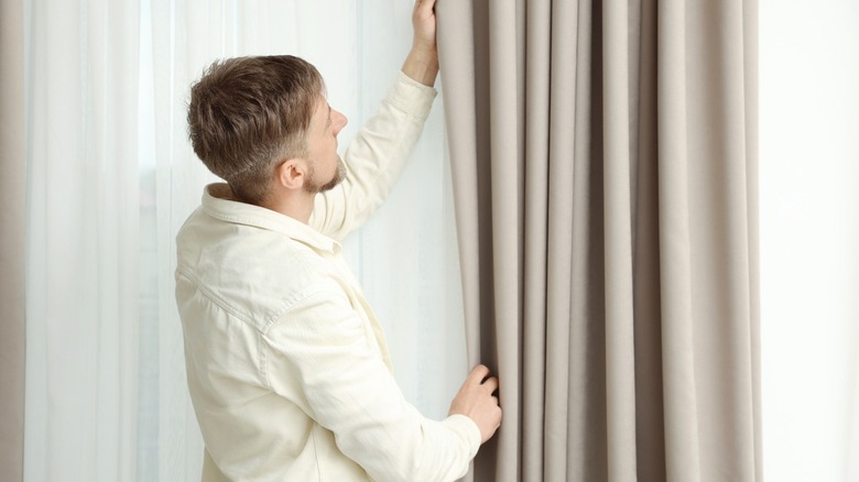 Man opening heavy curtains covering window