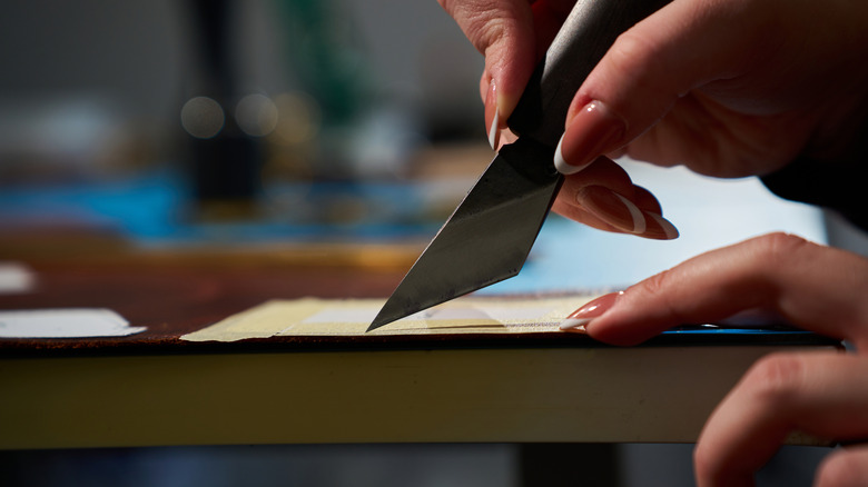A person uses a utility knife to make a precise cut