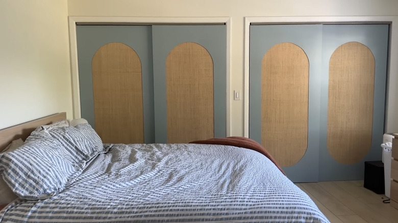 A bed sits in front of four light blue paneled closet doors