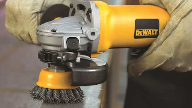Worker polishing metal with a DeWalt angle grinder and knotted brush attachment