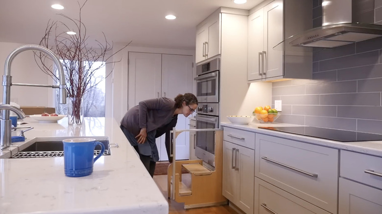 woman folding down a pull-out step stool installed between her cabinet and oven surround