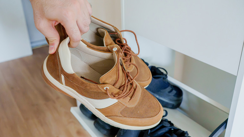 A man holding sneakers that he's placing in a white shoe rack