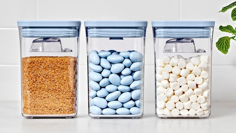 Three Oxo POP Containers filled with candies sit on a white kitchen countertop next to a potted plant