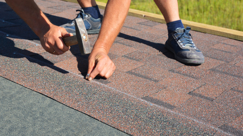 A worker installs asphalt shingles on a roof.