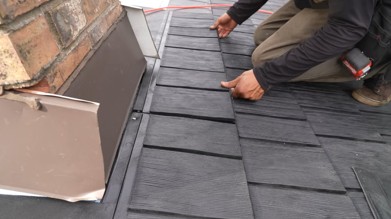 Man installing rubber shingles on the roof of a home near the chimney.