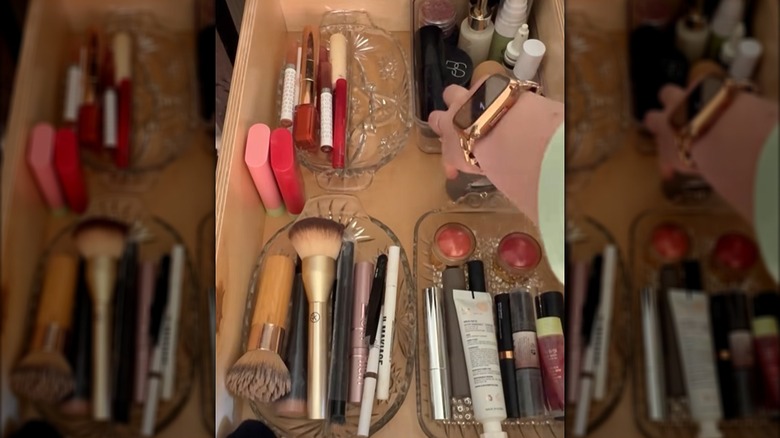 Person arranging toiletries in vintage glass containers inside a bathroom drawer