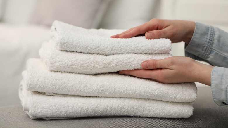 Woman stacking soft towels on bench near bed indoors