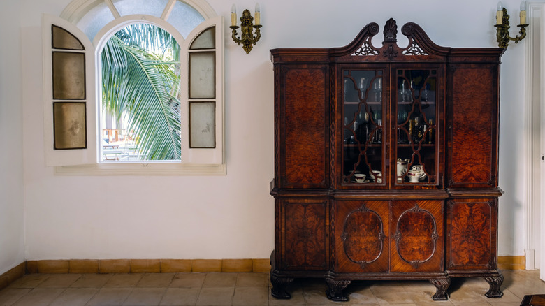 A large, vintage hutch in an empty room next to open windows