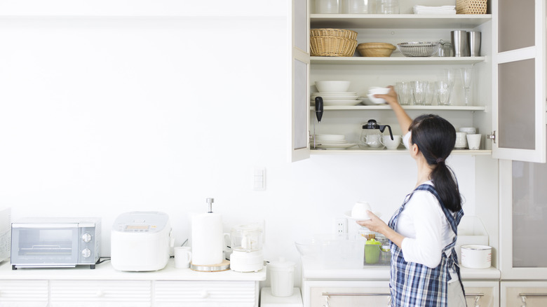 Woman putting away mugs in clean, minimalist kitchen