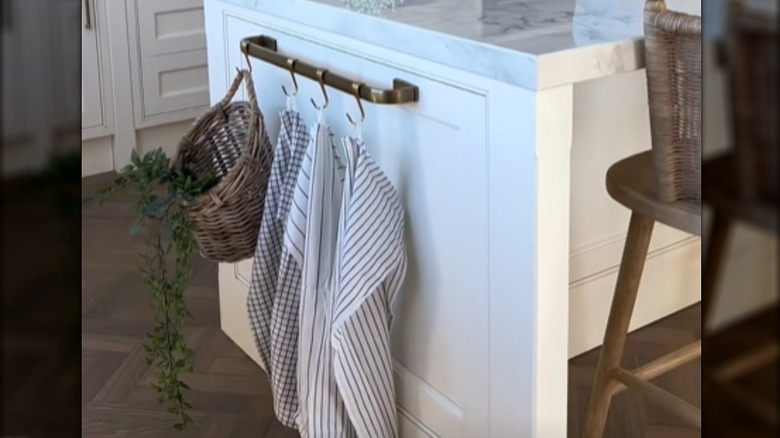 Towel bar with hooks on the side of a kitchen island holding towels and a basket