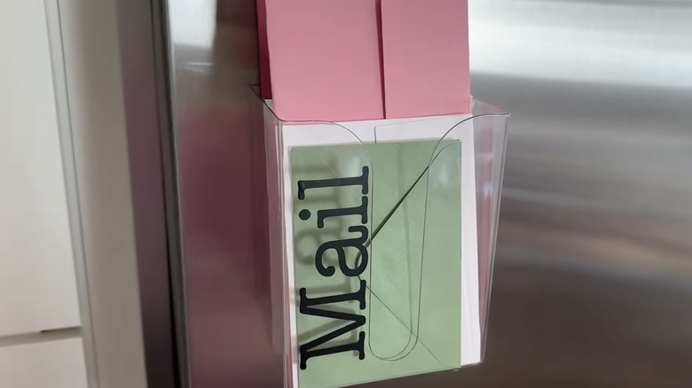 A clear Dollar Tree magnetic dryer sheet holder with the word "mail" on it and letters inside fastened to the refrigerator